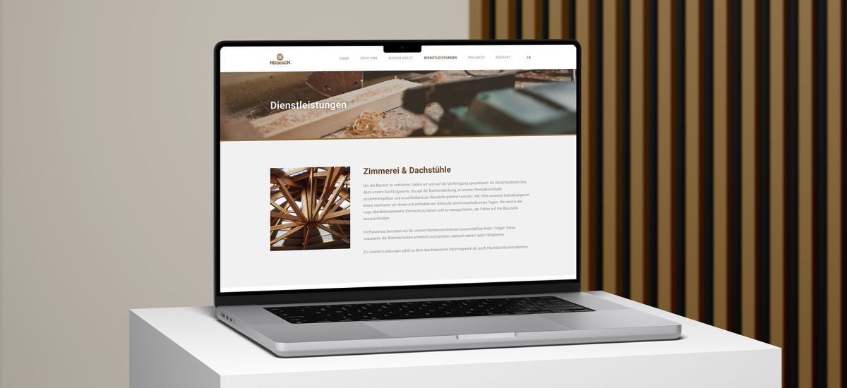 Macbook vor einem Holzlamellen-Hintergrund, auf dem die Dienstleistungsseite der Website von Holzbau Heidesch zu sehen ist.