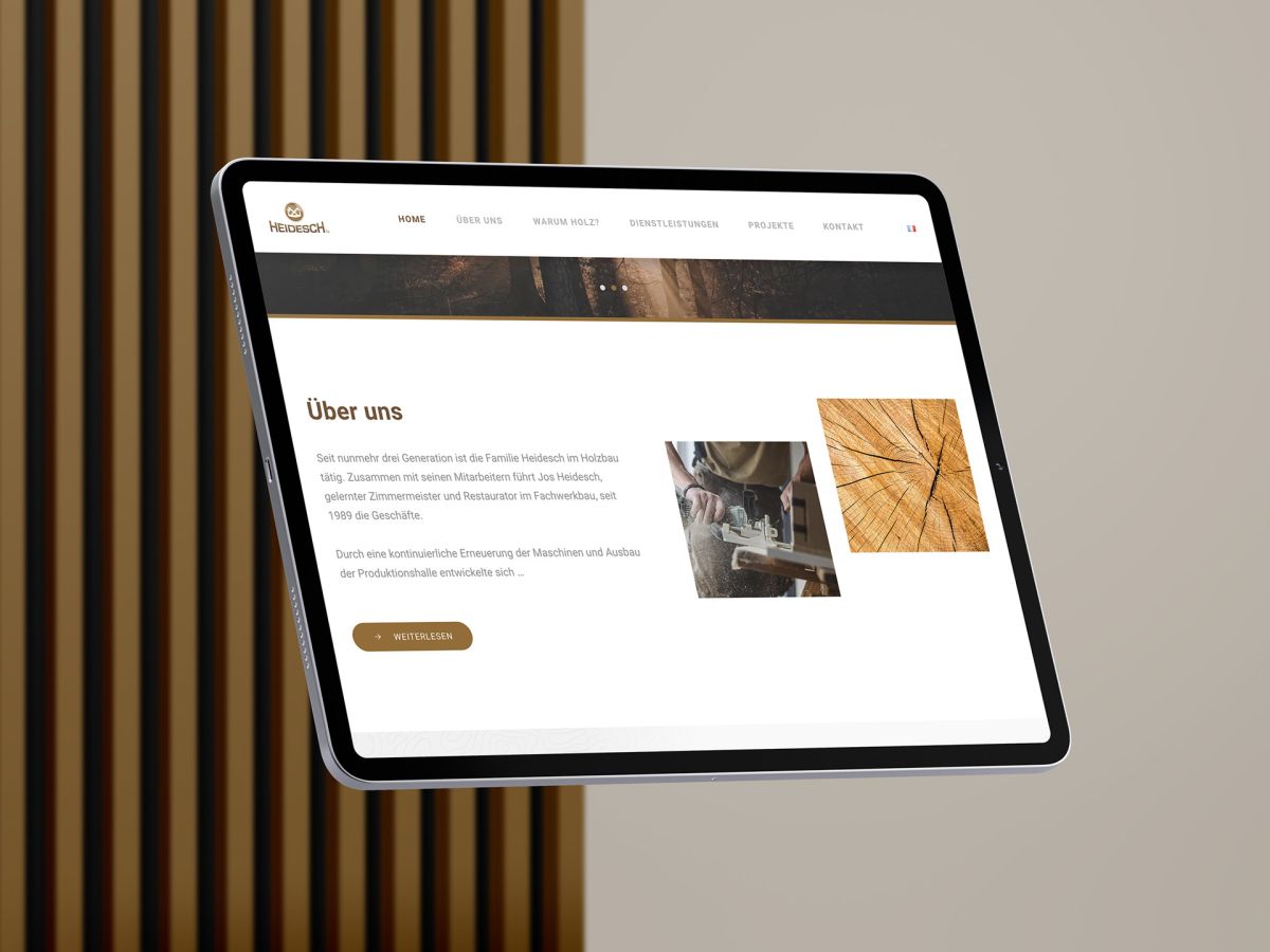 iPad vor einem Holzlamellen-Hintergrund, der den Abschnitt "Über uns" der Holzbau Heidesch Website zeigt.