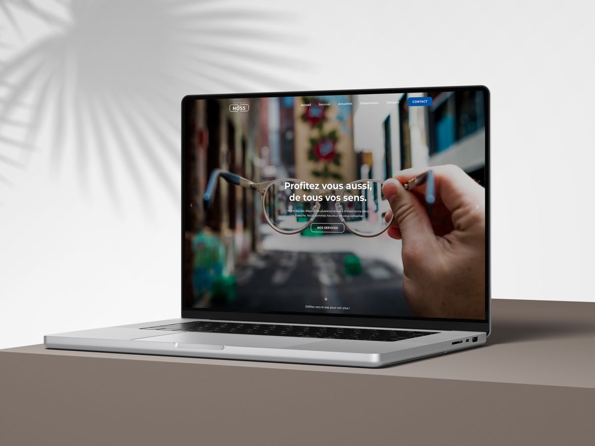 MacBook on a table showing the homepage of the Optique Hoss website.