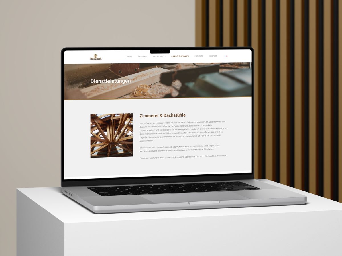 Macbook vor einem Holzlamellen-Hintergrund, auf dem die Dienstleistungsseite der Website von Holzbau Heidesch zu sehen ist.