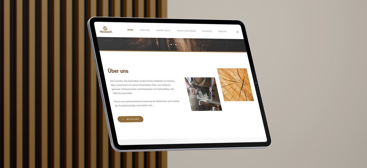 iPad in front of wooden lamellae background showing the "About us" section of the Holzbau Heidesch website.