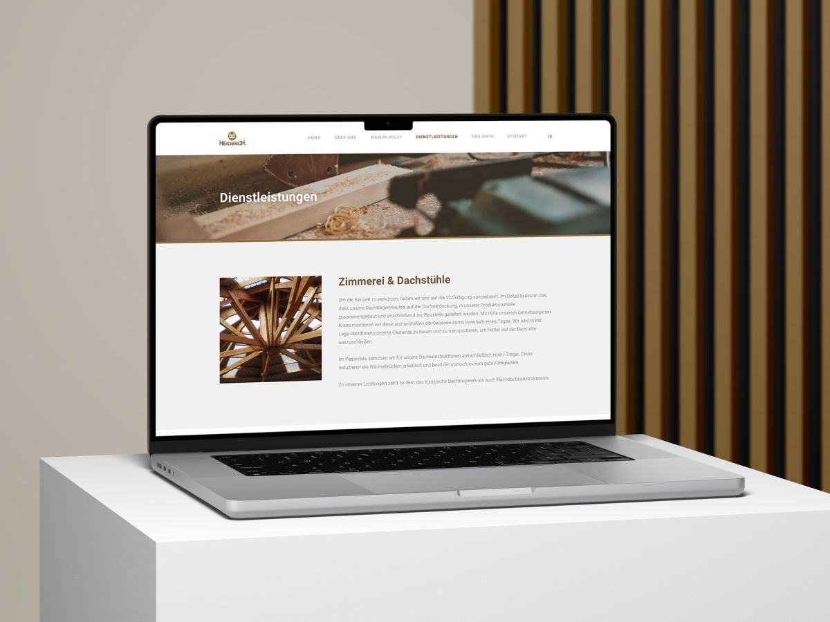 Macbook in front of a wooden lamellae background showing the services page of the Holzbau Heidesch website.