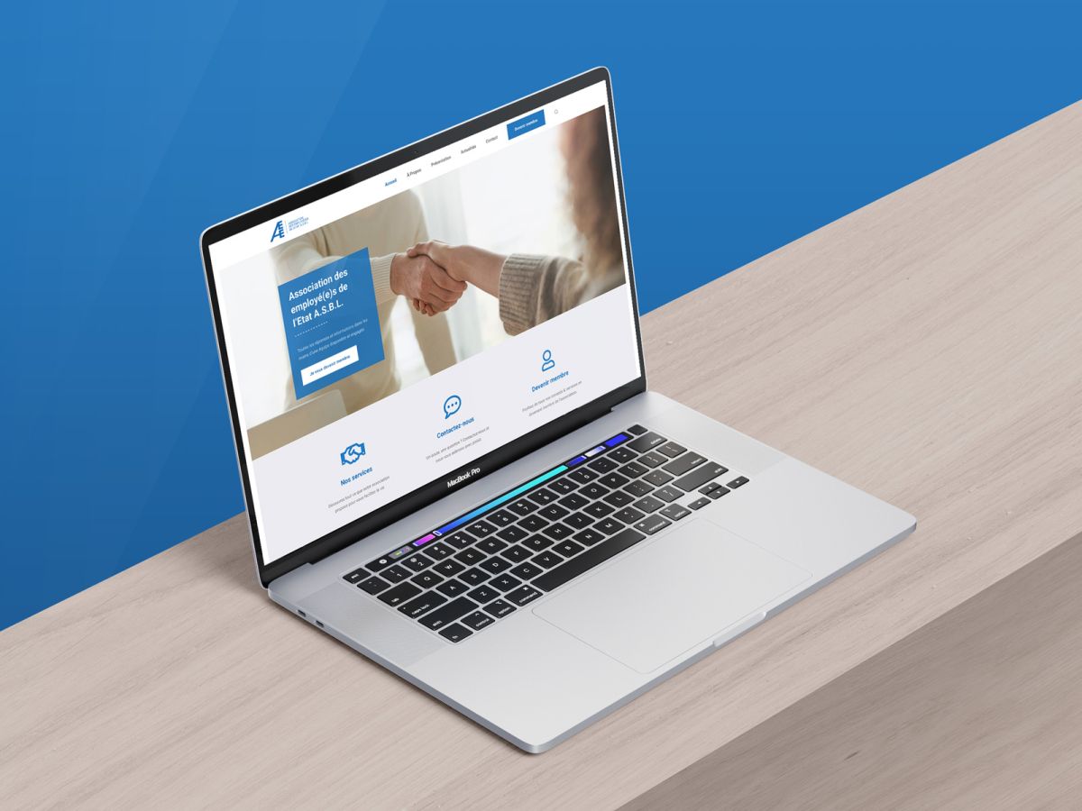 MacBook auf Holzuntergrund mit blauem Hintergrund, der die Homepage der AEE ASBL-Website zeigt.