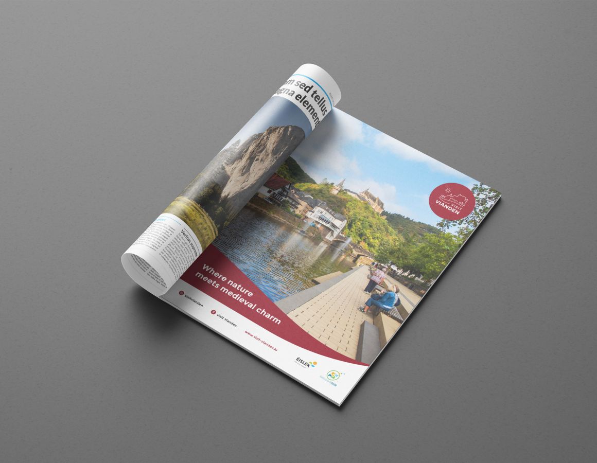 Din A4 große Anzeige für Visit Vianden, die die Promenade, den Fluss, die Brücke und das Schloss zeigt.
